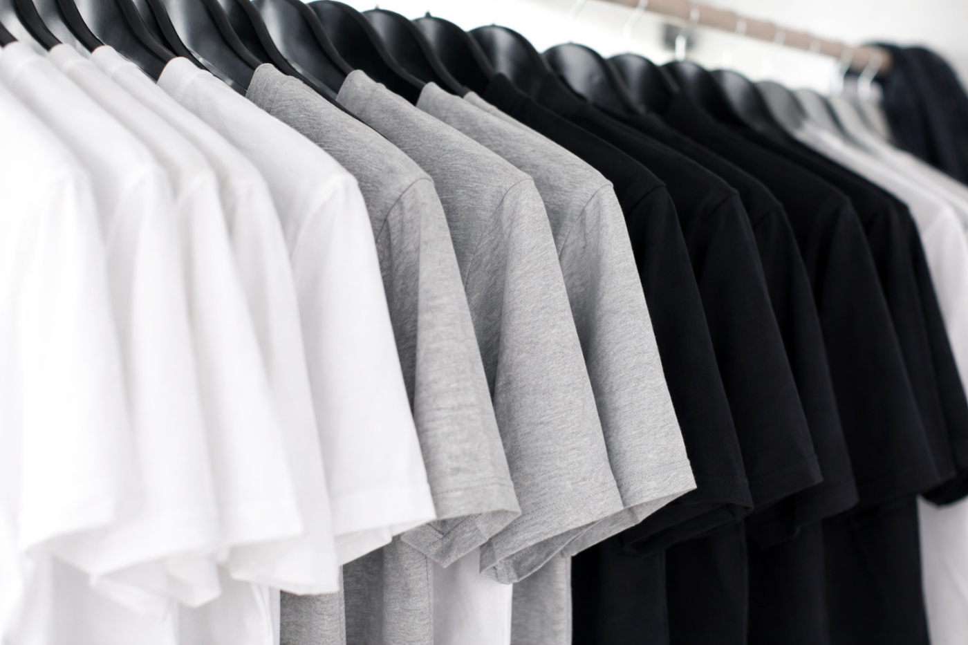 Row of white, gray, and black t-shirts on a rack.